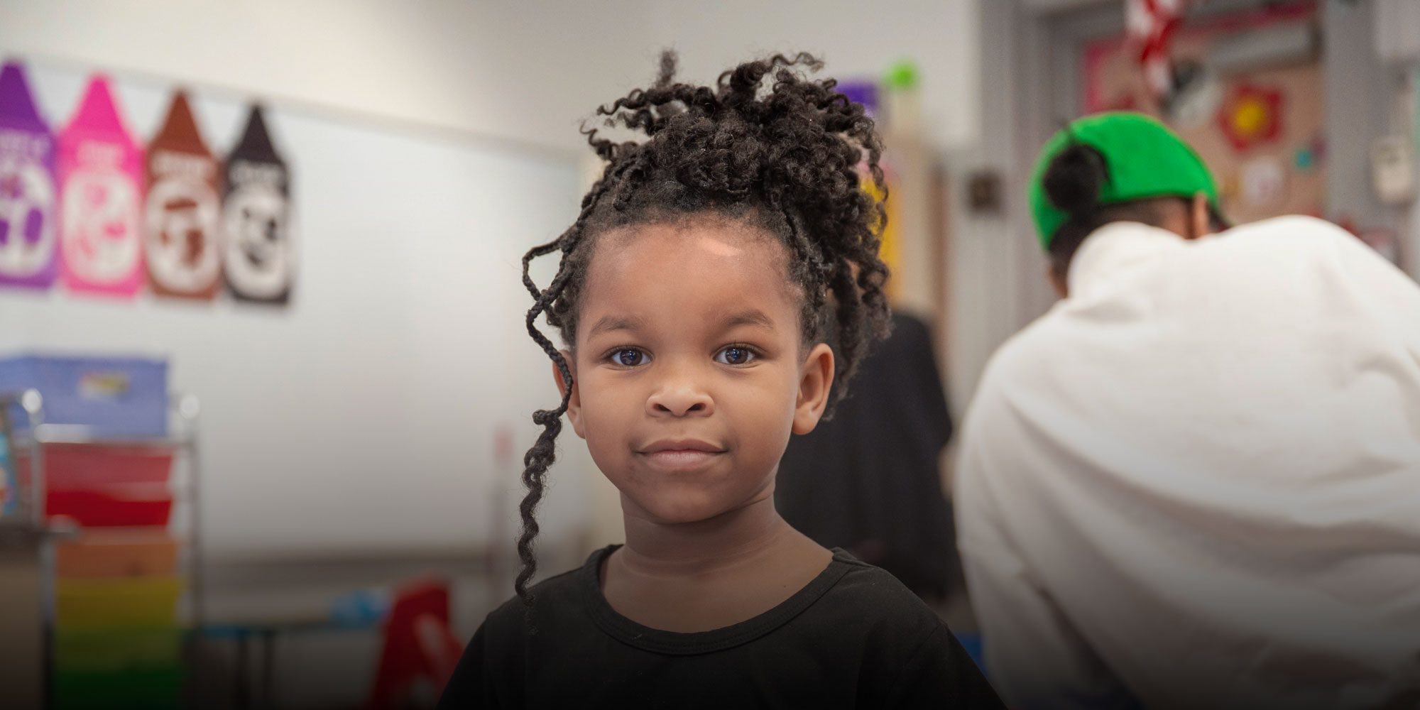 Young student with curly hair looking at the camera in a classroom.