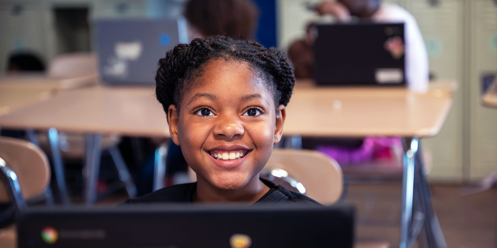 Smiling student sitting behind a laptop in a classroom.